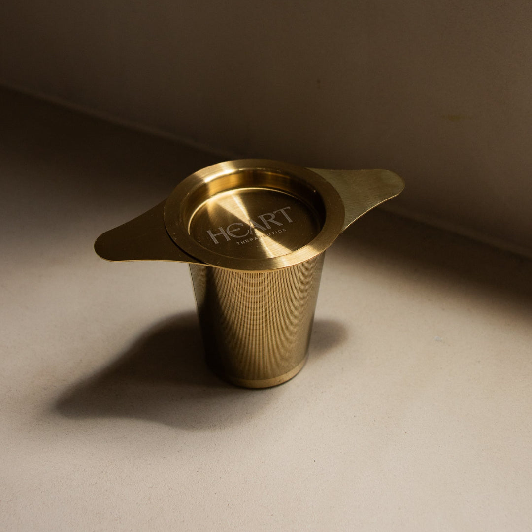 Gold metal Tewa infuser with 'HART' branding on a beige surface.