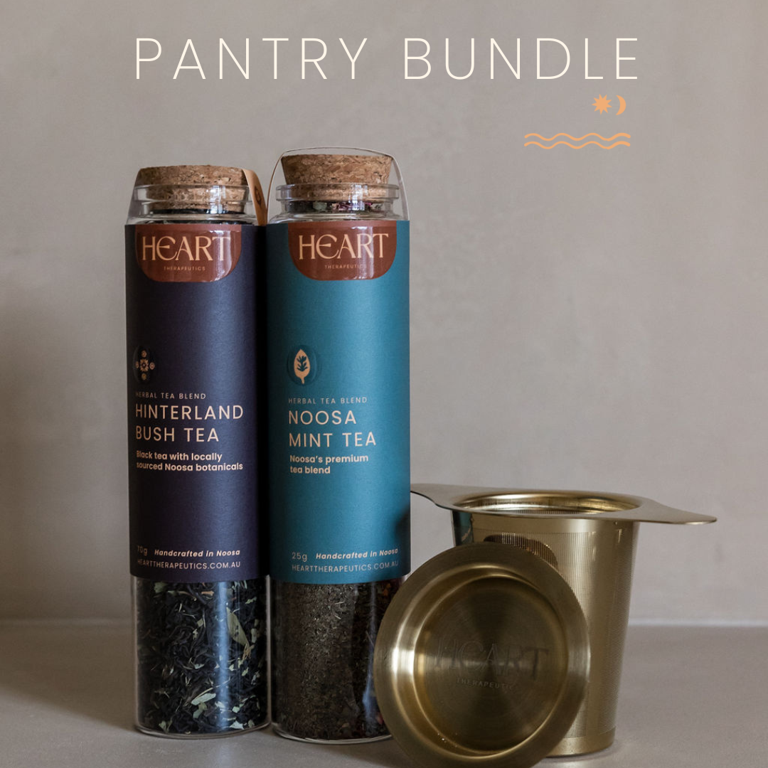 Two tea canisters labeled 'Hinterland Bush Tea' and 'Noosa Mint Tea' with a brass tea infuser on a neutral background.
