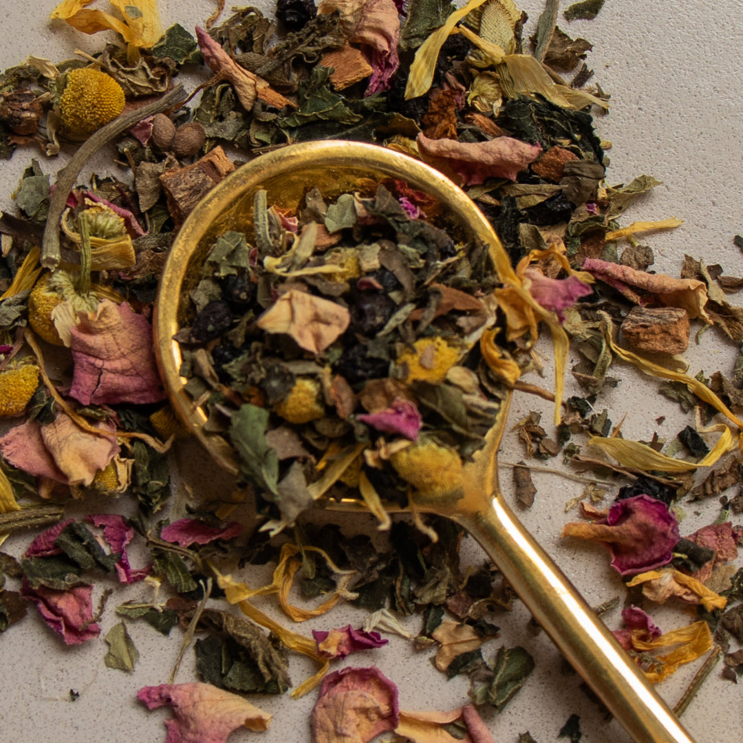Gold spoon amidst a pile of colorful dried herbs and flowers on a light background