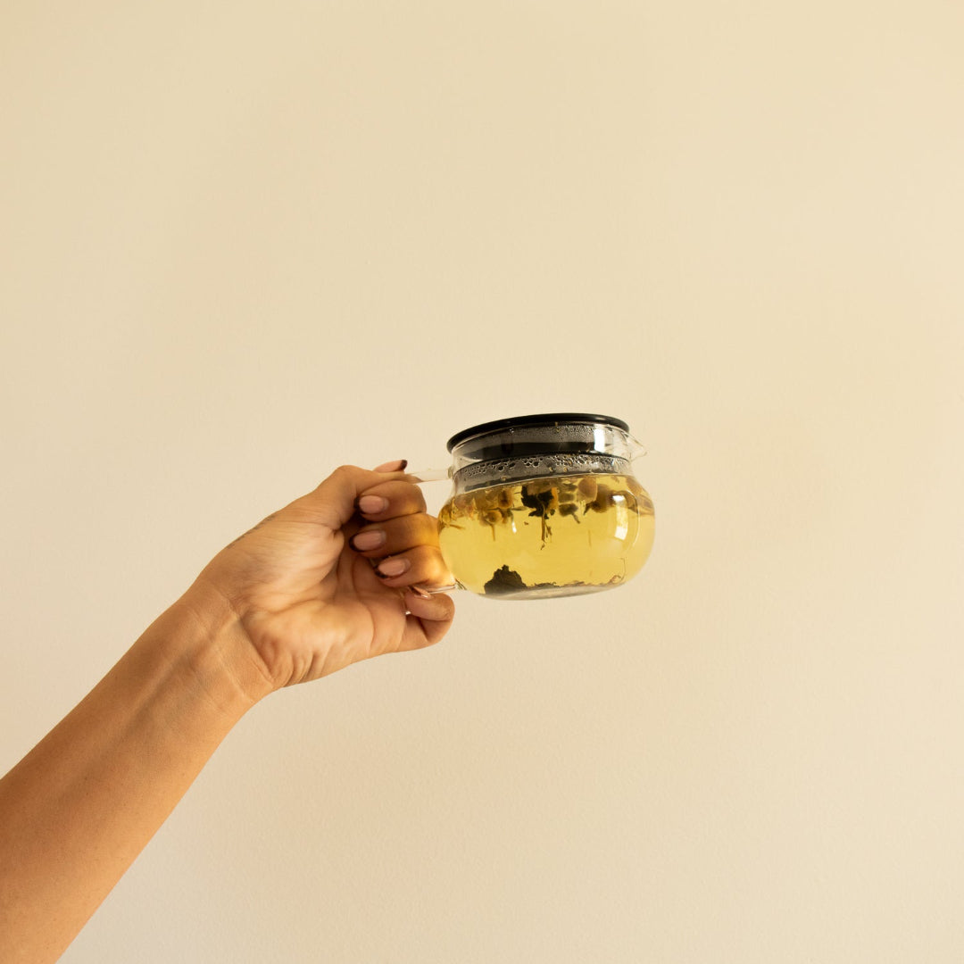 Hand holding a glass jar of yellow liquid against a beige background