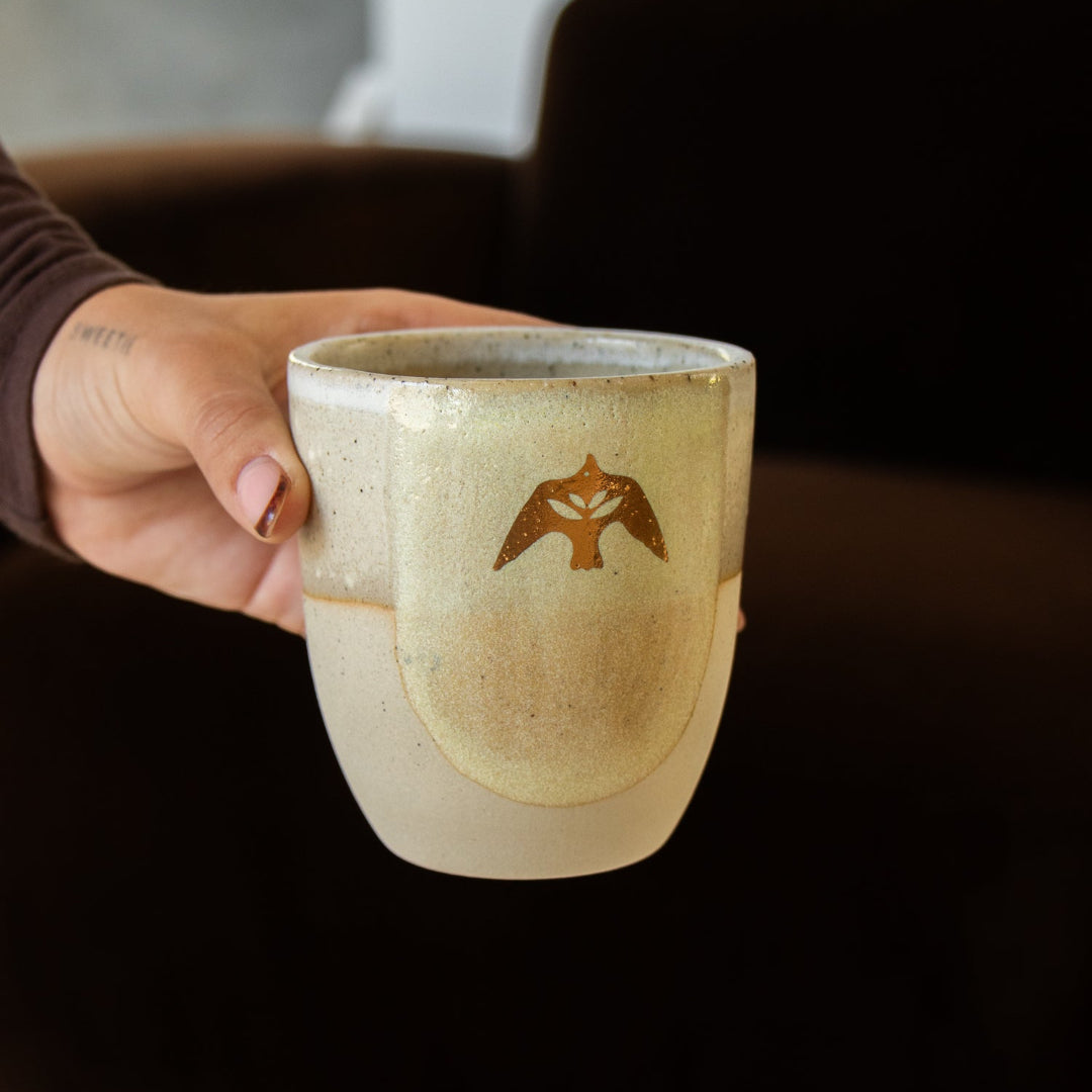 Hand holding a Heart Therapeutics gold icon ceramic cup with the bird design