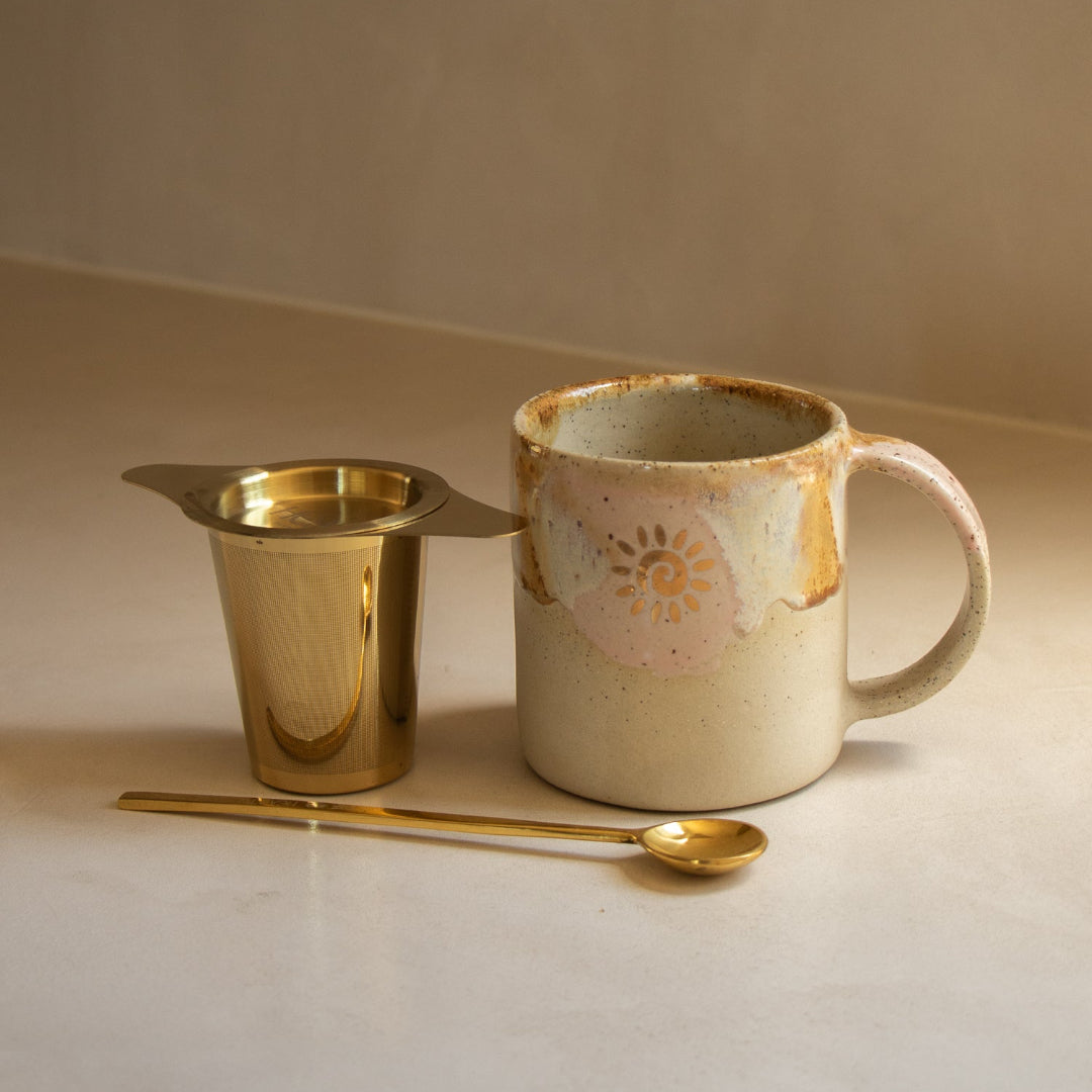 Ceramic mug with gold spoon and small container on a neutral background
