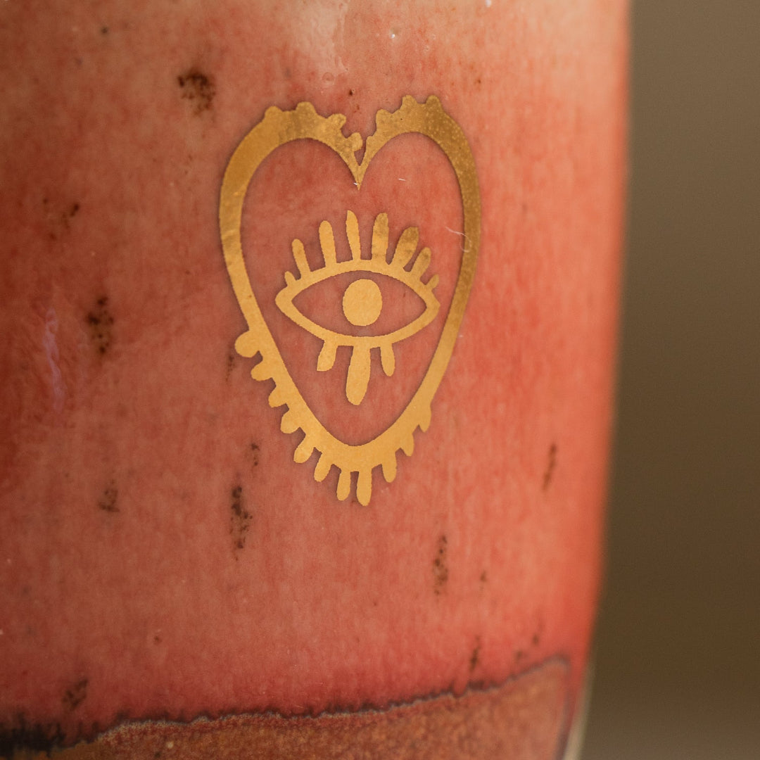 Ceramic mug with a gold heart design featuring an eye on a brown background