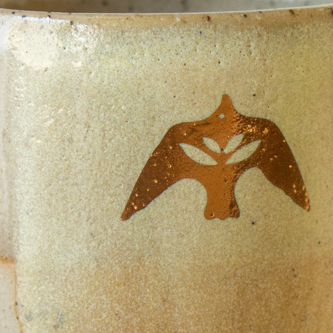 Close-up of a ceramic mug with a brown leaf design on a beige background