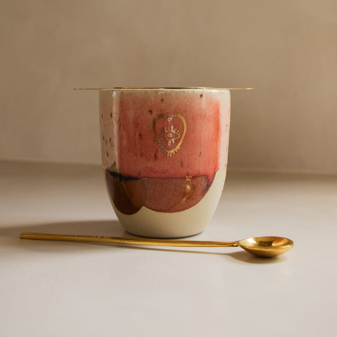 Ceramic cup with a gold spoon on a neutral background