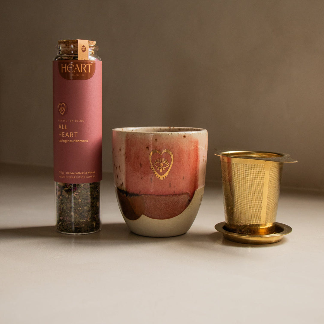Tea-making set with pink teapot, gold strainer, and pink canister on a neutral background