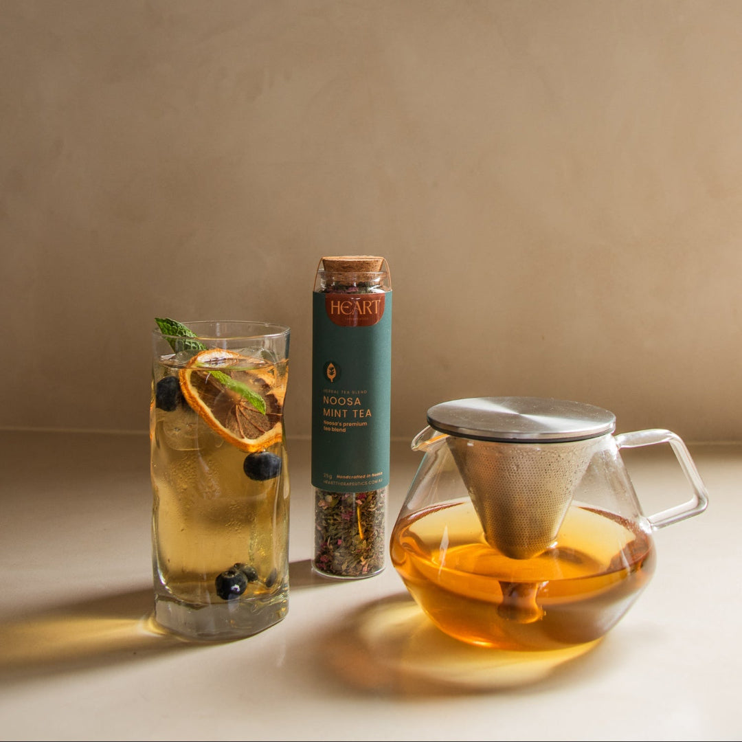 Tea-making setup with a glass of iced tea, loose leaf tea packaging, and a teapot on a beige surface.